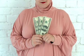 Wall Mural - Young muslim woman in pink hijab clothes hold of cash money in dollar banknotes and rosary in her hands