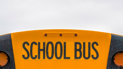 Wall Mural - Panorama Close up of the back side of a yellow school bus against homes and cloudy sky