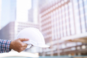 Close up of engineering male construction worker hand holding give safety white helmet for the safety of the work operation. outdoor of building background.