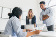 © Look! - African office worker in checkered shirt standing with arms crossed and looking at asian manager. Indoor portrait of freelance web-developers discussing something and using laptops.