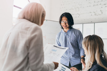 Wall Mural - Portrait from back of short-haired blonde female manager analysing reports and graphs. Indoor photo of international students preparing for exam in Economics.