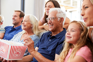 Wall Mural - Multi-Generation Family Sitting On Sofa At Home Eating Popcorn And Watching Movie Together