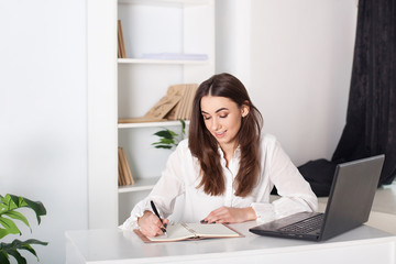 Happy smiling young girl working in the office. The girl writes in a notebook. Close-up portrait of an office worker. Positive young manager working on business project in office. business woman.