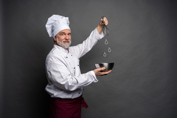 Wall Mural - Smiling mature male chef with bowl and mixer in hands on black background.