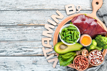 Wall Mural - Foods that contain natural vitamin B9: Liver, avocado, broccoli, spinach, parsley, beans, nuts, on a white wooden background. Top view.