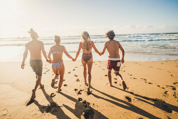 Wall Mural - Group of young people friend have fun at the beach in summer holiday vacation running from sand to sea water together in friendship - youthful happy couples enjoy the sunny day with ocean