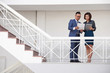 © DragonImages - Asian business couple standing on staircase of modern office and comparing document with online document on digital tablet
