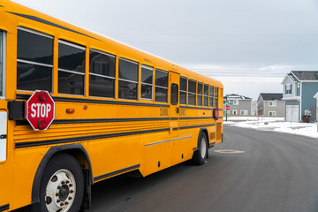 Wall Mural - Side view of a school bus on a road passing through snowy homes in winter