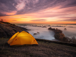 Wall Mural - orange illuminated from inside tent above river at sunset