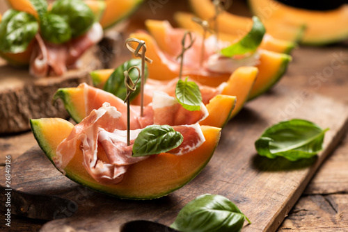 Fotomural Sliced melon with ham and basil leaves, served on a wood chopping board