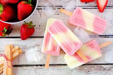 Healthy strawberry yogurt summer popsicles, above view table scene against a white wood background