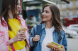 © Yakobchuk Olena - Two happy female friends walking with hot dogs