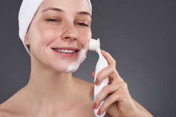 Sticker - Smiling young woman with freckles using pore cleansing brush after bath