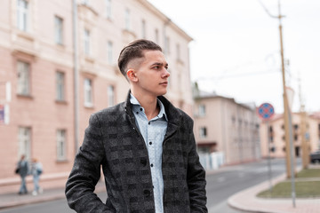 Business handsome young man with a fashionable hairstyle in a luxurious checkered jacket in an elegant shirt walks around the city near vintage buildings on a warm spring day. Successful modern guy.