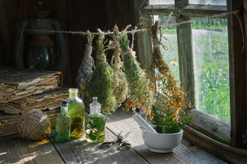 Wall Mural - Tincture or infusion bottles, old books, mortar and hanging bunches of dry medicinal herbs. Herbal medicine.