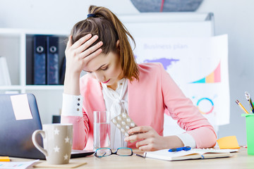 young beautiful business woman boss feeling sick and tired, sitting at her workplace and taking pill