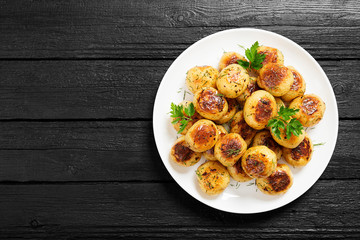 Wall Mural - Roasted new potato in white plate on black wooden background.