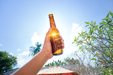 Vacation concept. Male hand holding bottle of beer against sunny sky.