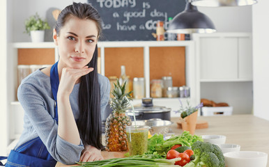 Wall Mural - Happy young woman in kitchen with fresh vegetables on the table