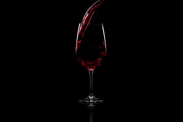 Red wine pouring into a wine glass, over black background, horizontal image