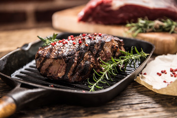 Wall Mural - Grilled beef steak in grill pan with herbs rosemary on wooden table