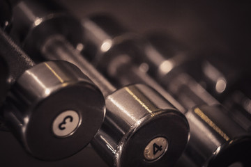 hand metal dumbbells lie together in a row on the rack in the gym close-up. training tools