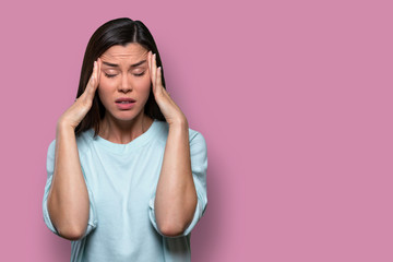 woman overwhelmed with stress and concern, confusion and doubt, hands to head, on pink background co