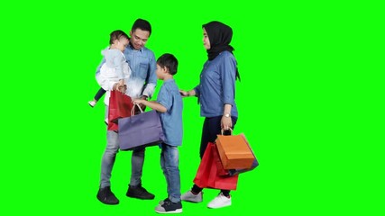 Wall Mural - Full length of happy muslim family holding shopping bags with gift in the studio. Shot in 4k resolution with green screen background