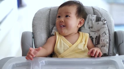 Wall Mural - Father feeding porridge to his kid on baby feeding seat. The baby enjoy eating  meal and looking with smiling to father. Baby healthcare and family activity concept.