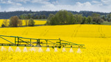 Fototapeta  - Agricultural sprayer detail. Flowering rapeseed field. Brassica napus. Working spraying machine in yellow canola land. Spring landscape. Chemical fertilizers, toxic pesticides, insecticides. Ecology.