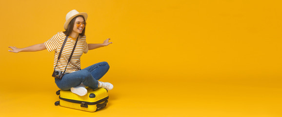 European Caucasian woman sitting on suitcase and spreading arms as if she is flying, concept of travelling, isolated