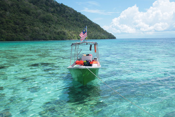 A white boat with a Malaysia flag, on green water beach