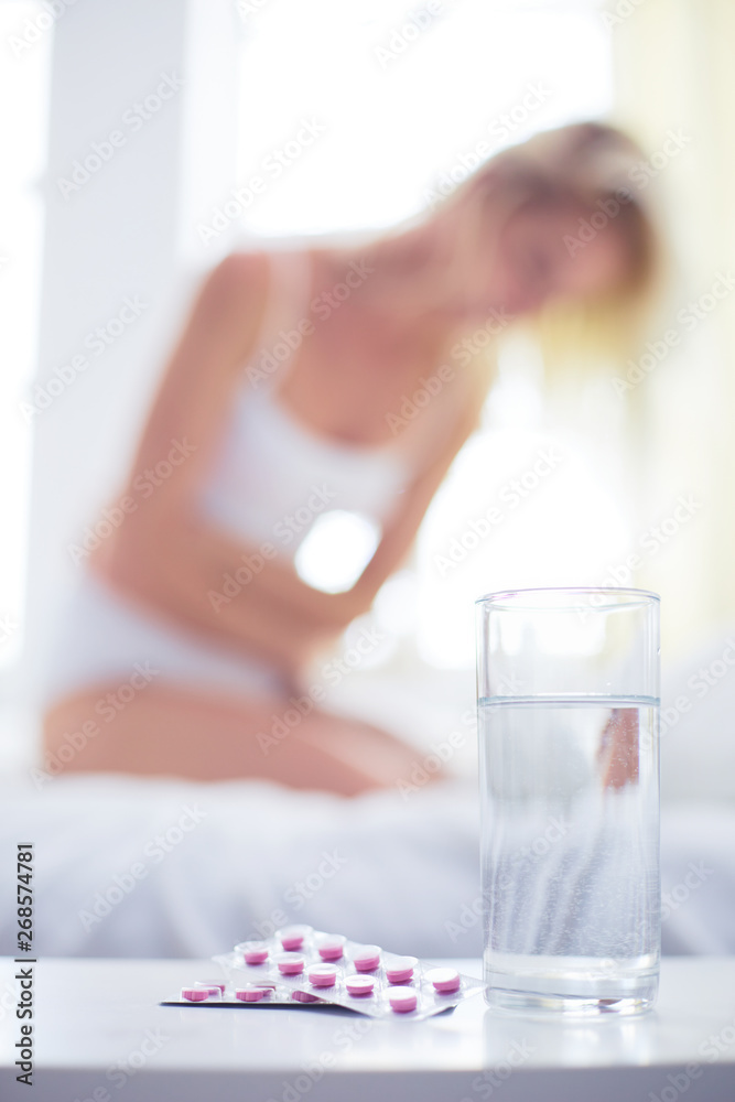 Young beautiful woman with pills lying on bed in bedroom - obrazy, fototapety, plakaty 