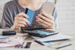 © doucefleur - woman hand calculating  her expenses and debt from credit cards with smart phone