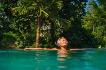 Wall Mural - attractive and happy middle aged Asian woman relaxed at tropical resort infinity swimming pool with jungle background enjoying relaxed in luxury holidays trip