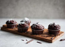 Chocolate Cupcakes Decorated With A Chocolate Cream Frosting With Coconut Powder On Top And Chocolate Shavings On A Rustic Wooden Board On Light Background.