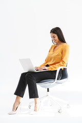 Wall Mural - Portrait of cute young businesswoman sitting in chair and using laptop while working in bright office