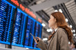 © geargodz - woman using smartphone with flight information board at airport