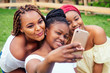© yurakrasil - portrait of three beautiful african-american women afro braids dreadlocks and turban taking pictures of yourself on the phone in the park at a picnic,sisters on vacation