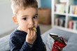 © Miljan Živković - Portrait of a little small boy eating unhealthy snacks potato chips at home