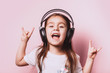 Cute little girl listening music wearing headphones on pink background. Funny emotions. Copyspace for text.