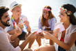 © NDABCREATIVITY - Group of young friends having fun while playing cards on beach