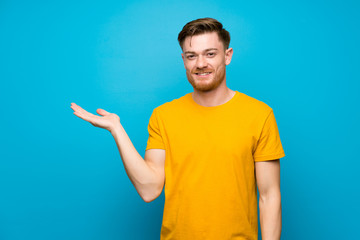 Redhead man over blue wall holding copyspace imaginary on the palm to insert an ad