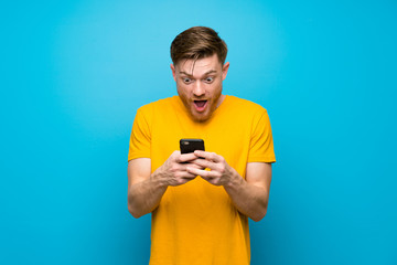 Redhead man over blue wall surprised and sending a message