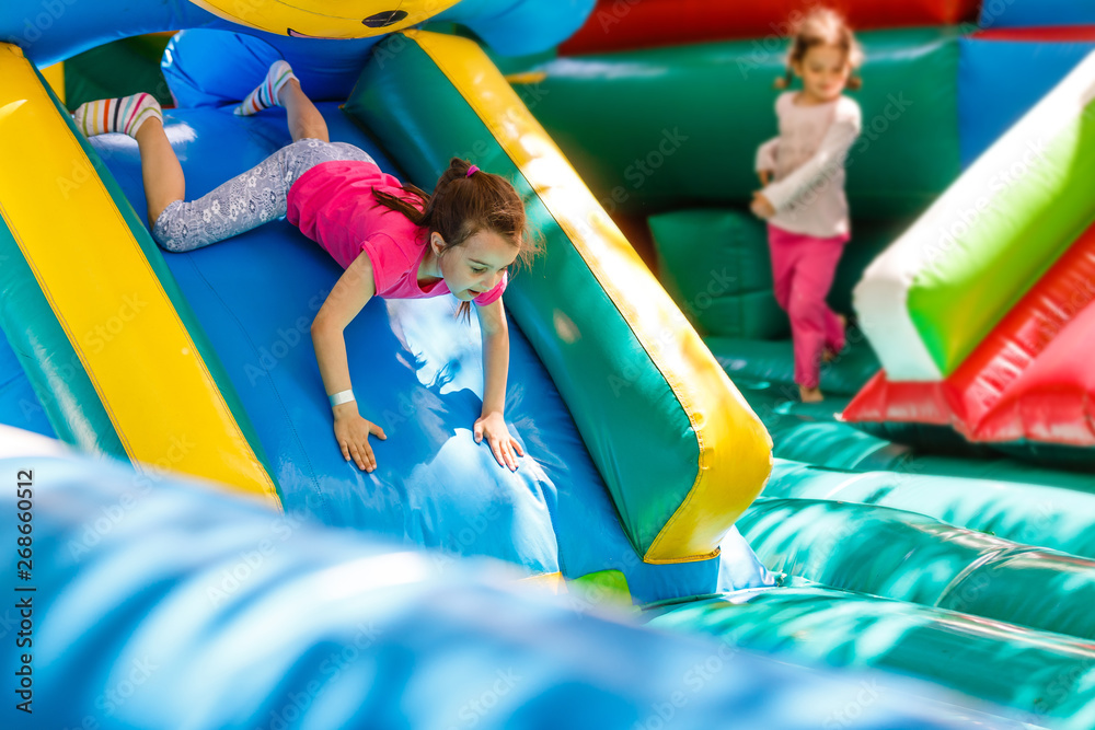 Child jumping on colorful playground trampoline. Kids jump in inflatable bounce castle on kindergarten birthday party Activity and play center for young child. Little girl playing outdoors in summer - obrazy, fototapety, plakaty 