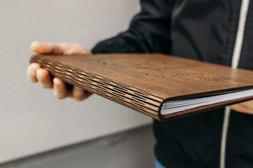 Wall Mural - Man holds Photobook in a wooden cover. Guy holds notebook with plywood cover