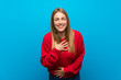 Woman with red sweater over blue wall smiling a lot