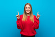 Woman with red sweater over blue wall pointing up a great idea