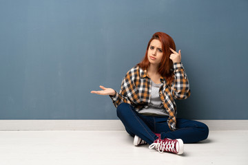 Young redhead woman sitting on floor making the gesture of madness putting finger on the head