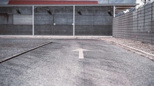 Asphalt Road With Selective Focus On A White Arrow Road Marking On It Following To Concrete Wall In A Defocused Background, Fencing On The Right, Shallow Depth Of Field, Lisbon, Portugal